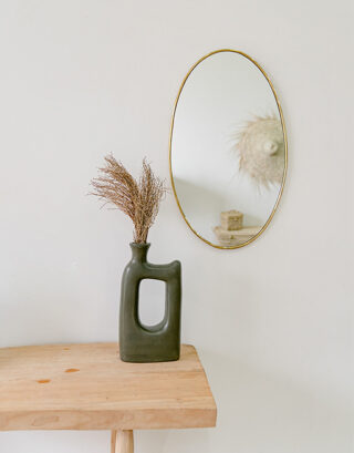 Miroir ovale accroché au mur près d'un vase avec des fleurs séchées