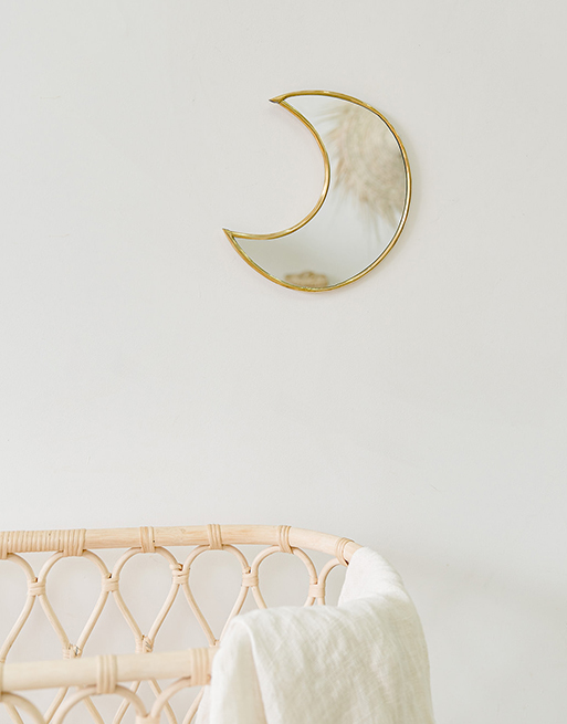 Miroir lune accroché au mur près d'un joli berceau en rotin