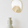 Miroir galet petit format accroché au mur près d'un vase blanc posé sur une table en bois