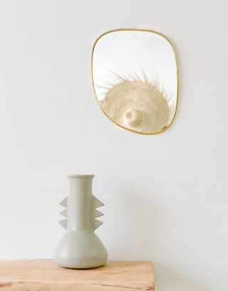 Miroir galet petit format accroché au mur près d'un vase blanc posé sur une table en bois