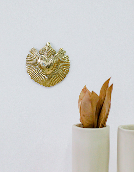 Coeur en laiton décoratif inspiration ex-voto accroché au mur près d'un vase