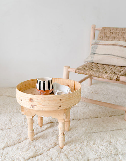 Table ronde en bois posé sur un tapis blanc près d'un fauteuil en paille