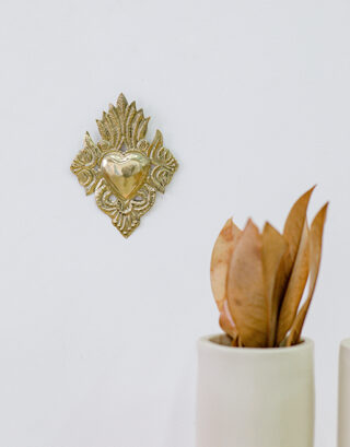 Cœur ex-voto accroché au mur près d'un vase avec feuilles séchées