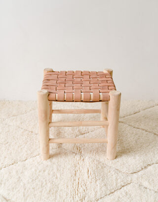 Petit tabouret en cuir marocain posé sur un tapis blanc