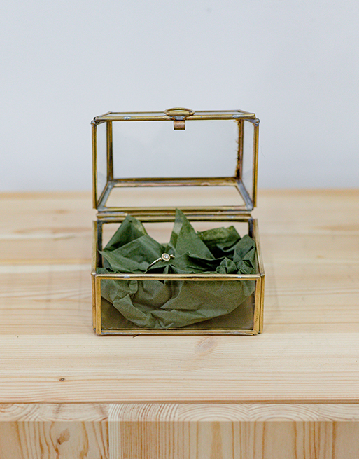 Boîte à bijoux haute en verre ouverte avec une bague à l'intérieur posée sur de papier de soie