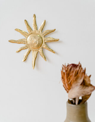 Soleil martelé en laiton accroché au mur près d'un vase avec une fleur séchée