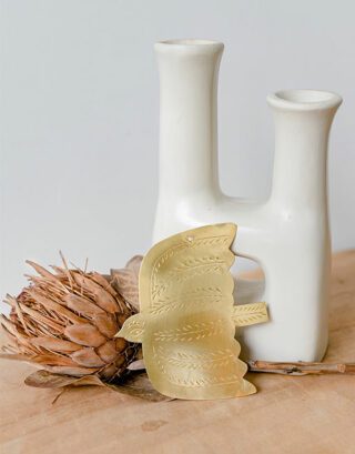 Oiseau doré en laiton martelé posé contre un vase avec fleur séchée