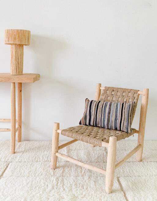 Notre coussin Haïk aux rayures fines posé sur une fauteuil en paille dans un décor naturel