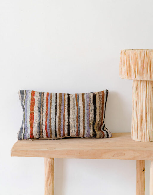 Notre coussin vintage rayé posé sur une table en bois près d'une lampe raphia