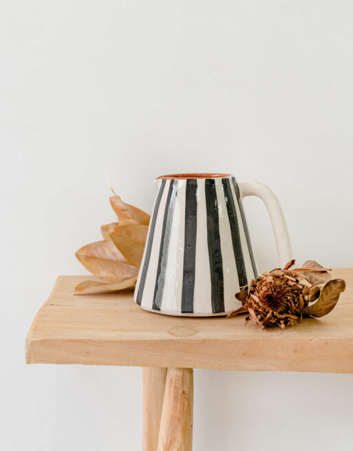 Notre carafe rayée noire posée sur une table en bois dans un décor naturel de fleurs séchées.