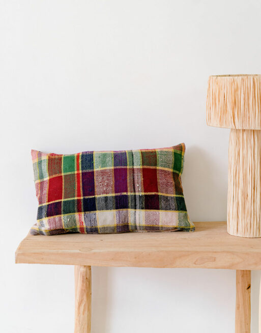 Notre coussin à carreaux bordeaux posé sur une table près d'une jolie lampe en raphia