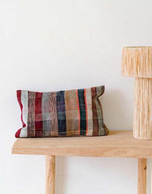 Notre coussin ancien aux rayures chaudes posé sur une table près d'une jolie lampe en raphia