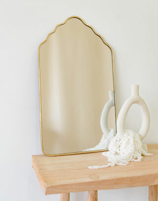 Notre miroir doré forme arche posé contre un mur près d'un vase agrémenté de fleurs séchées