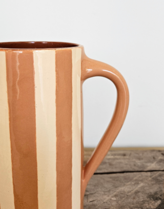 Notre carafe rose rayée posée sur une planche en bois près d'une fleur séchée