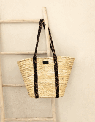 Notre panier Alya avec ses anses imprimées léopard, accroché à une échelle en bois